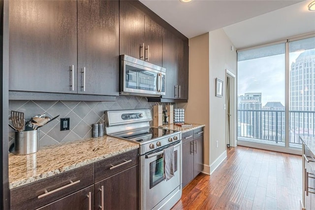 kitchen featuring dark hardwood / wood-style floors, decorative backsplash, appliances with stainless steel finishes, dark brown cabinets, and light stone counters