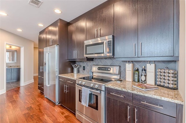 kitchen featuring light stone countertops, appliances with stainless steel finishes, decorative backsplash, dark brown cabinetry, and light hardwood / wood-style floors