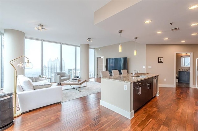 kitchen with sink, light stone counters, dark hardwood / wood-style floors, decorative light fixtures, and a kitchen island with sink