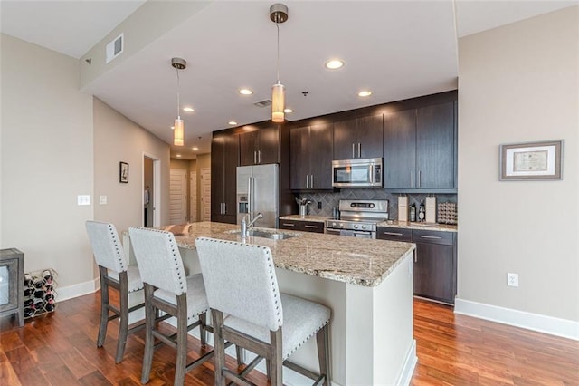 kitchen featuring a kitchen island with sink, pendant lighting, stainless steel appliances, and wood-type flooring