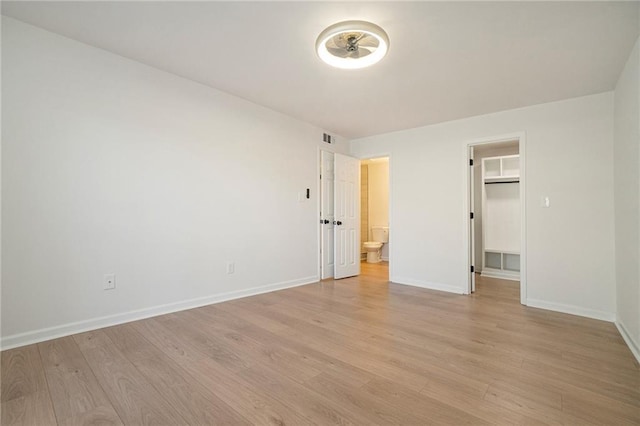 unfurnished bedroom with ensuite bath, a walk in closet, a closet, and light hardwood / wood-style flooring