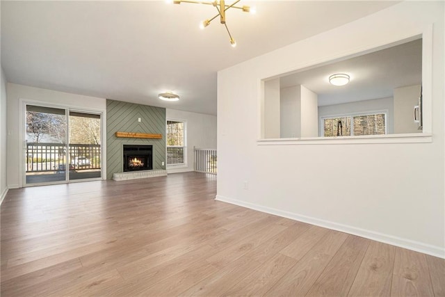 unfurnished living room featuring light wood-type flooring, a large fireplace, and an inviting chandelier