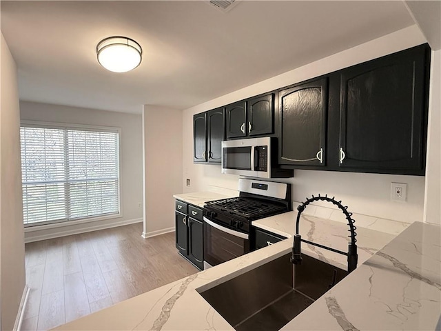 kitchen with light stone countertops, appliances with stainless steel finishes, light hardwood / wood-style flooring, and sink