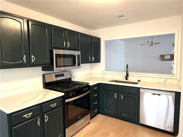 kitchen featuring light wood-type flooring, light stone countertops, stainless steel appliances, and sink