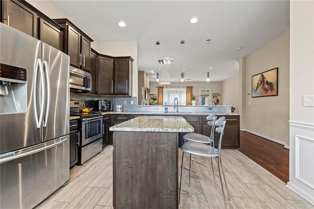 5440 Willow Oak Dr, Norcross, GA 30092 - kitchen featuring appliances with stainless steel finishes, a peninsula, dark brown cabinets, a kitchen island, and light stone countertops
