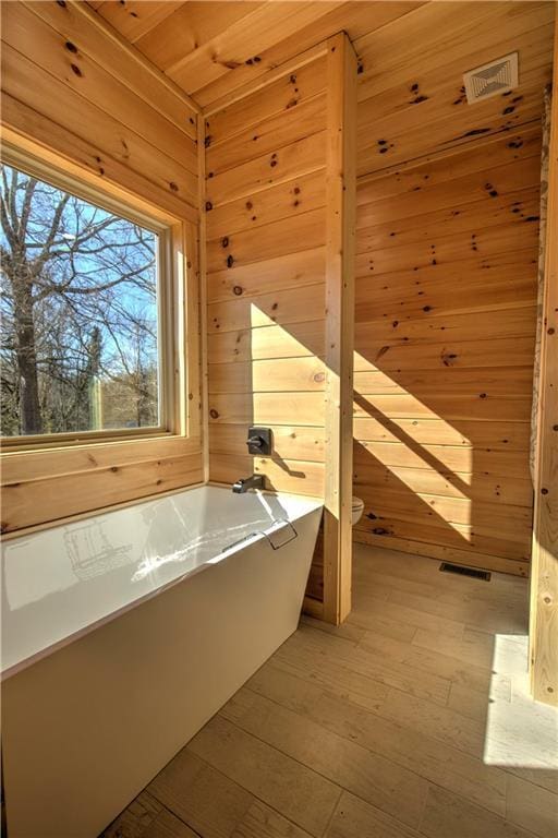 bathroom with wood ceiling, wood-type flooring, toilet, a bath, and wood walls