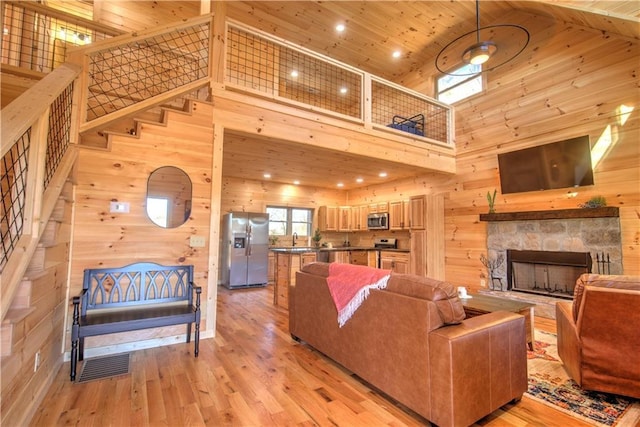 living room with wood ceiling, wood walls, a stone fireplace, high vaulted ceiling, and light hardwood / wood-style flooring