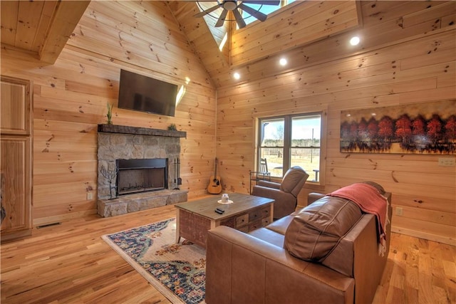 living room with ceiling fan, light hardwood / wood-style flooring, a stone fireplace, and high vaulted ceiling