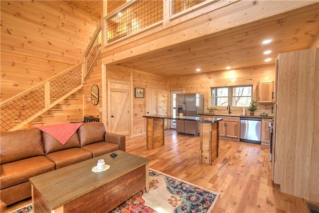 living room with a towering ceiling, sink, wooden walls, light hardwood / wood-style flooring, and wooden ceiling