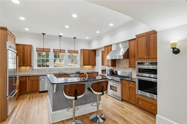 kitchen featuring a sink, stainless steel appliances, a kitchen breakfast bar, wall chimney exhaust hood, and a center island