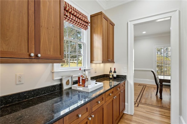 kitchen featuring dark stone countertops, baseboards, light wood-type flooring, ornamental molding, and brown cabinets