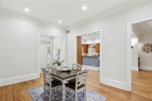 dining area with arched walkways, light wood-style flooring, baseboards, and ornamental molding