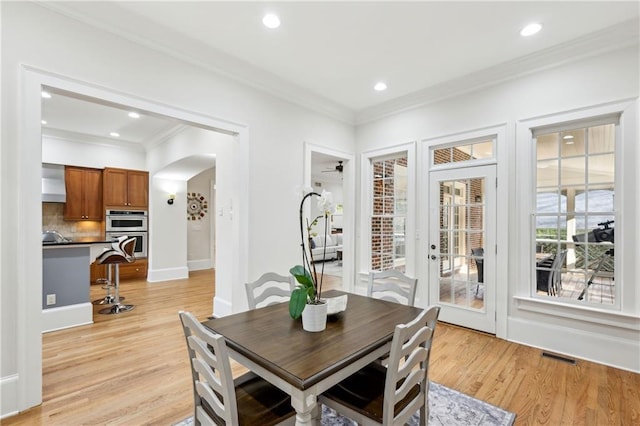 dining area featuring visible vents, light wood-style flooring, recessed lighting, arched walkways, and crown molding