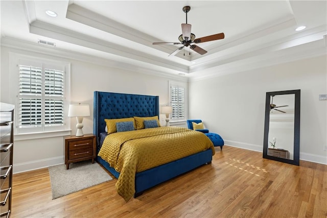 bedroom with visible vents, a raised ceiling, baseboards, and wood finished floors