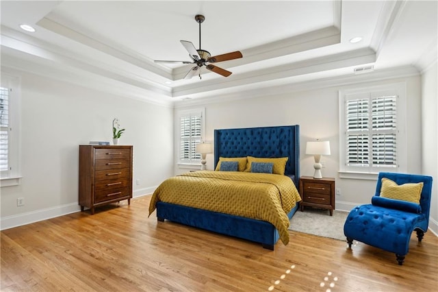 bedroom with light wood finished floors, visible vents, baseboards, a tray ceiling, and ornamental molding