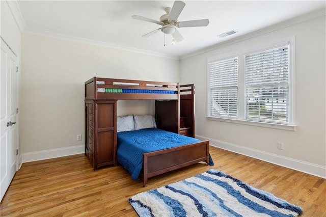 bedroom featuring baseboards, wood finished floors, visible vents, and ornamental molding