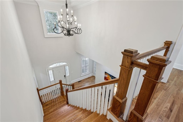 stairs featuring baseboards, a notable chandelier, a high ceiling, and wood finished floors