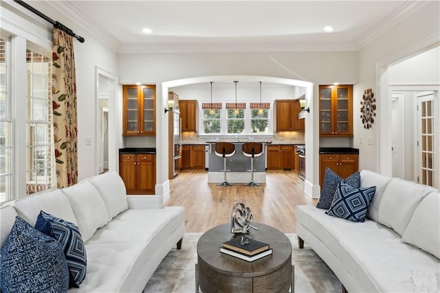 living room with recessed lighting, light wood-type flooring, arched walkways, and ornamental molding