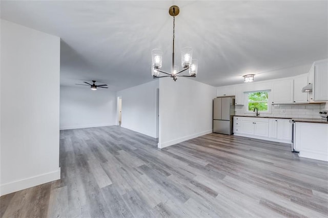 unfurnished living room with a ceiling fan, a sink, a chandelier, light wood-type flooring, and baseboards
