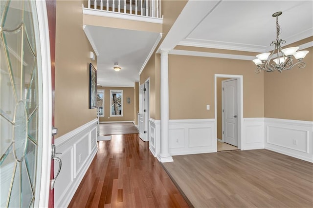 foyer entrance featuring an inviting chandelier, wood finished floors, crown molding, and ornate columns