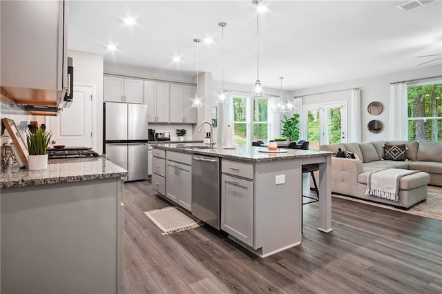 kitchen with decorative light fixtures, sink, a kitchen island with sink, light stone counters, and stainless steel appliances