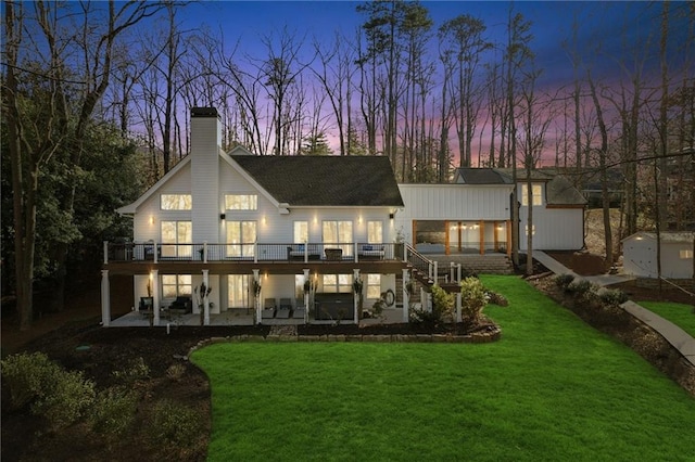 back house at dusk featuring a wooden deck, a yard, and a patio area