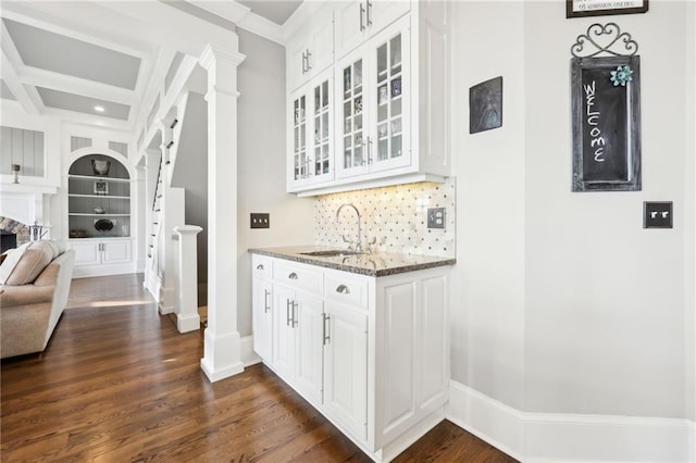 interior space featuring dark stone countertops, decorative columns, a sink, glass insert cabinets, and open floor plan