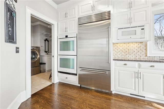 kitchen featuring light stone countertops, visible vents, washer / dryer, built in appliances, and white cabinetry