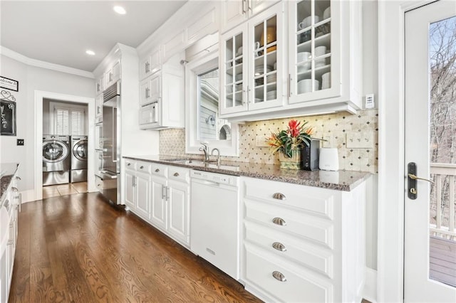 kitchen featuring independent washer and dryer, a sink, stone counters, glass insert cabinets, and built in appliances