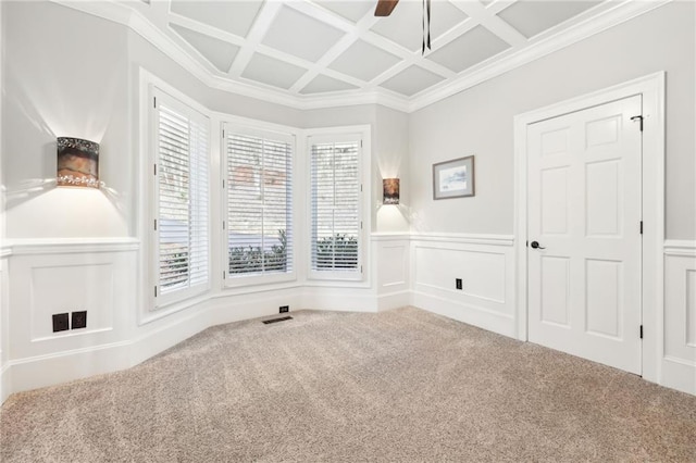 carpeted empty room with coffered ceiling, ceiling fan, wainscoting, crown molding, and a decorative wall