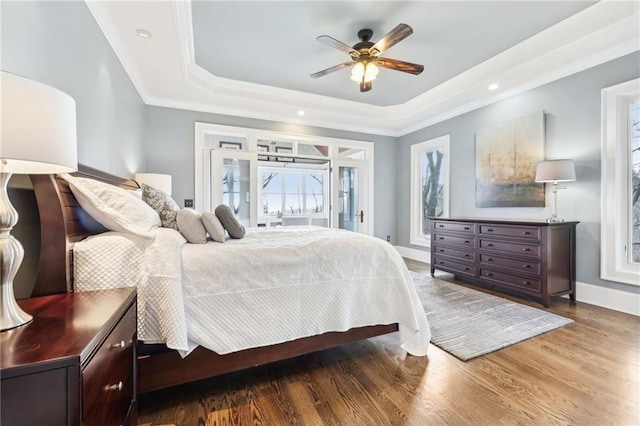 bedroom featuring crown molding, ceiling fan, baseboards, a tray ceiling, and wood finished floors