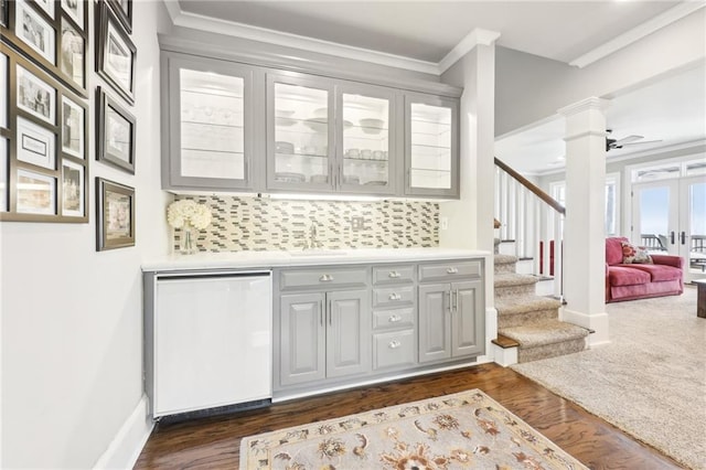 bar with ornate columns, white dishwasher, ornamental molding, stairs, and a sink