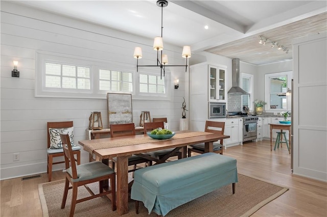 dining space featuring beam ceiling, rail lighting, a chandelier, light wood-type flooring, and visible vents