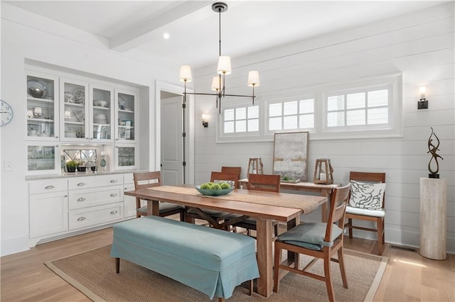 dining area with beamed ceiling, an inviting chandelier, a wealth of natural light, and light wood-type flooring