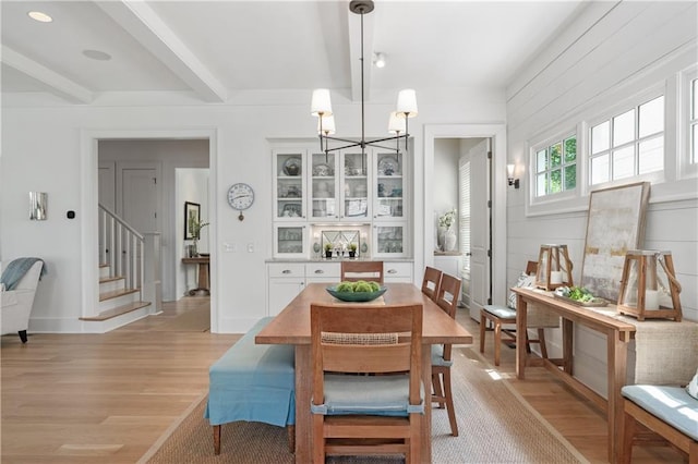 dining space featuring beamed ceiling, a chandelier, stairway, and light wood-style floors