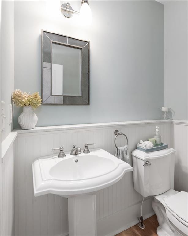 half bathroom with wood finished floors, a wainscoted wall, and toilet