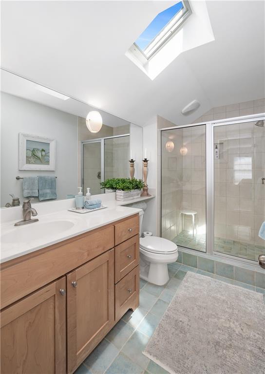 bathroom featuring vanity, toilet, tile patterned floors, vaulted ceiling with skylight, and a stall shower