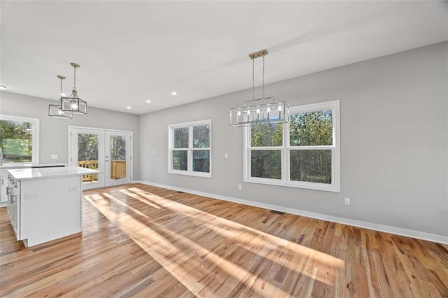 unfurnished dining area featuring light wood finished floors, baseboards, a wealth of natural light, and french doors