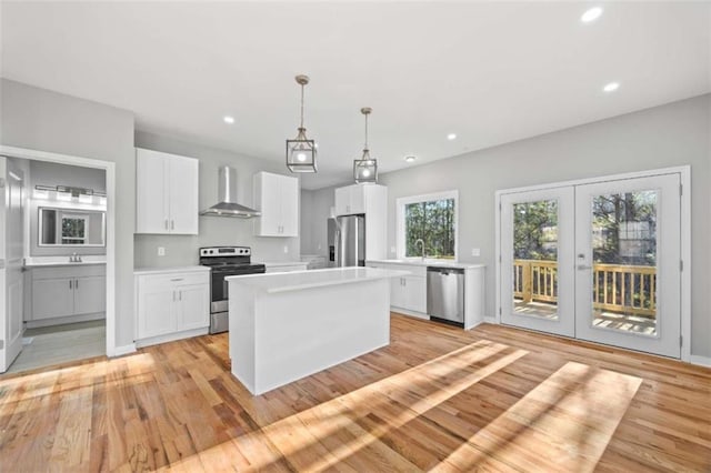 kitchen with white cabinets, wall chimney exhaust hood, a center island, stainless steel appliances, and light countertops