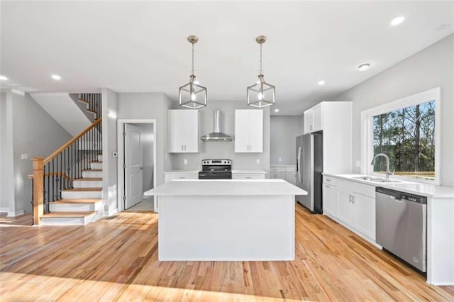 kitchen with a center island, stainless steel appliances, light countertops, a sink, and wall chimney range hood