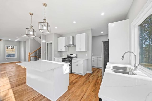 kitchen featuring light wood-style flooring, electric range, a sink, light countertops, and wall chimney range hood