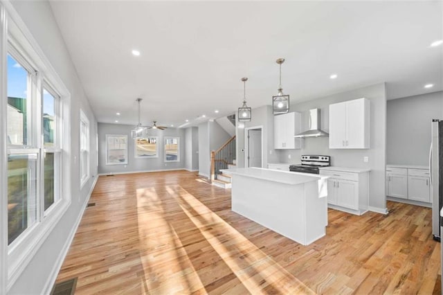 kitchen featuring white cabinets, wall chimney exhaust hood, a kitchen island, light wood-style flooring, and stainless steel range with electric stovetop