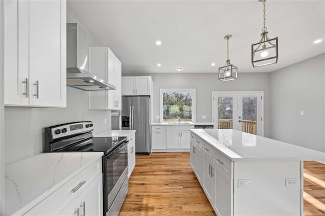 kitchen with appliances with stainless steel finishes, a center island, french doors, wall chimney range hood, and white cabinetry