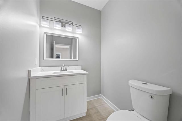 half bathroom with wood finished floors, vanity, toilet, and baseboards