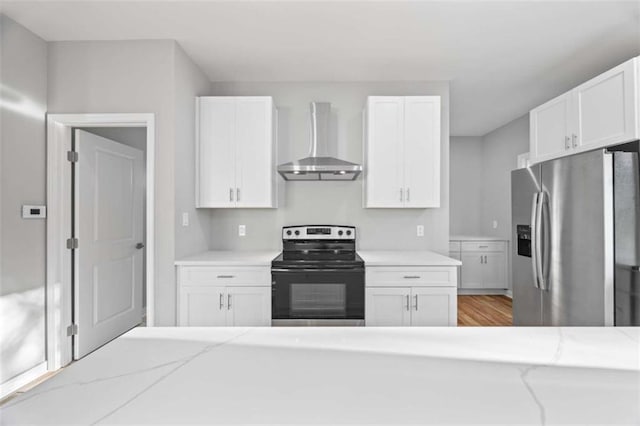 kitchen with light stone counters, range with electric cooktop, white cabinets, wall chimney exhaust hood, and stainless steel fridge