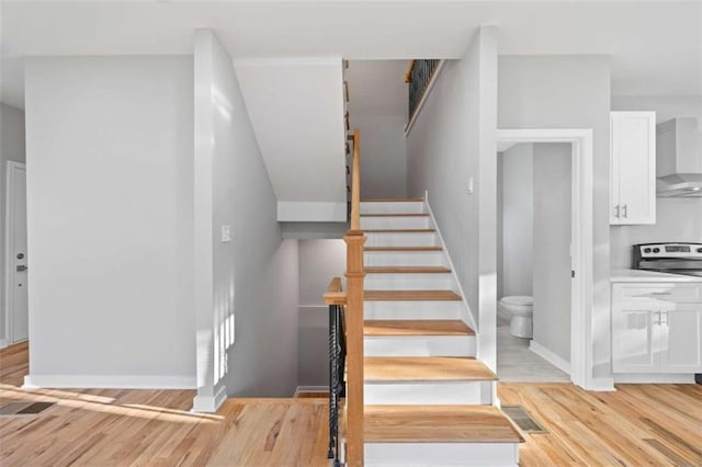 staircase with wood finished floors, visible vents, and baseboards