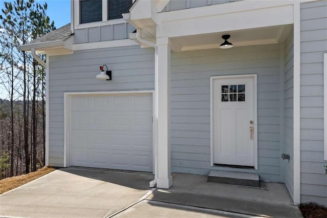 view of exterior entry featuring an attached garage, driveway, a shingled roof, and board and batten siding