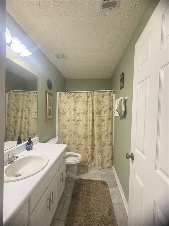 3484 Lynley Mill Ln, Dacula, GA 30019 - full bathroom with vanity, toilet, a textured ceiling, and tile patterned flooring
