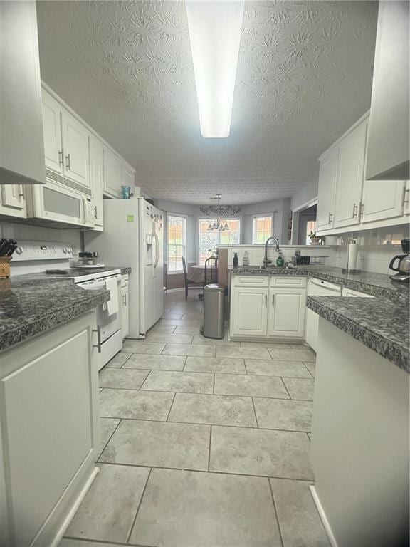 3484 Lynley Mill Ln, Dacula, GA 30019 - kitchen featuring white appliances, a peninsula, a textured ceiling, dark countertops, and white cabinets