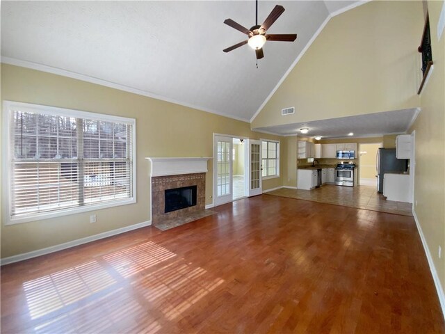 unfurnished living room featuring visible vents, ceiling fan, wood finished floors, a tile fireplace, and baseboards